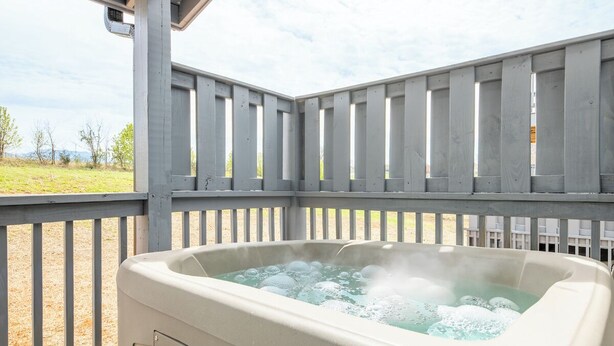 A hot tub in an outdoor setting with a wooden deck and a view of the landscape. - Modern 3BD Home Near TOWN! Hot Tub + Games + VIEWS (Sevierville)