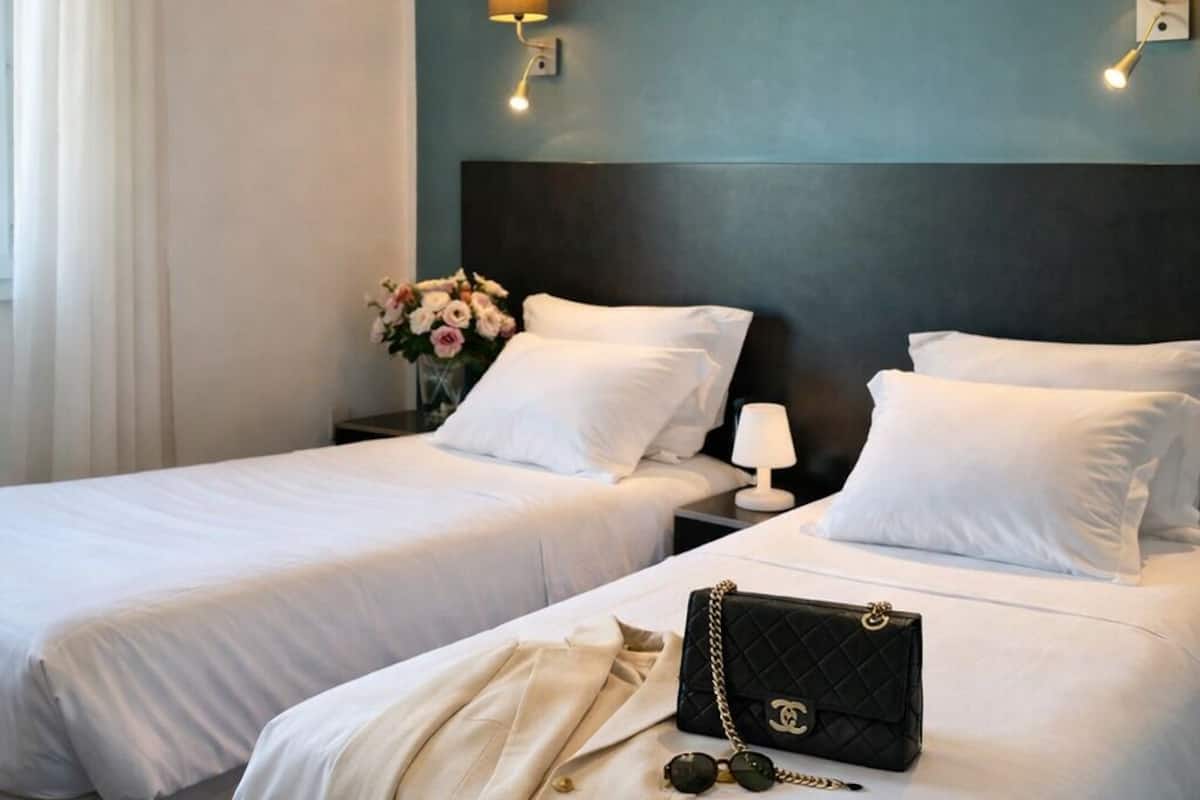 A hotel room with two beds, a nightstand, a lamp, and a decorative vase with flowers.