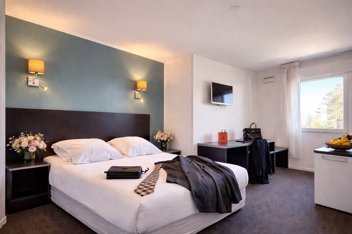 A hotel room with a bed, bedside tables, a desk, a chair, a TV, and a window.
