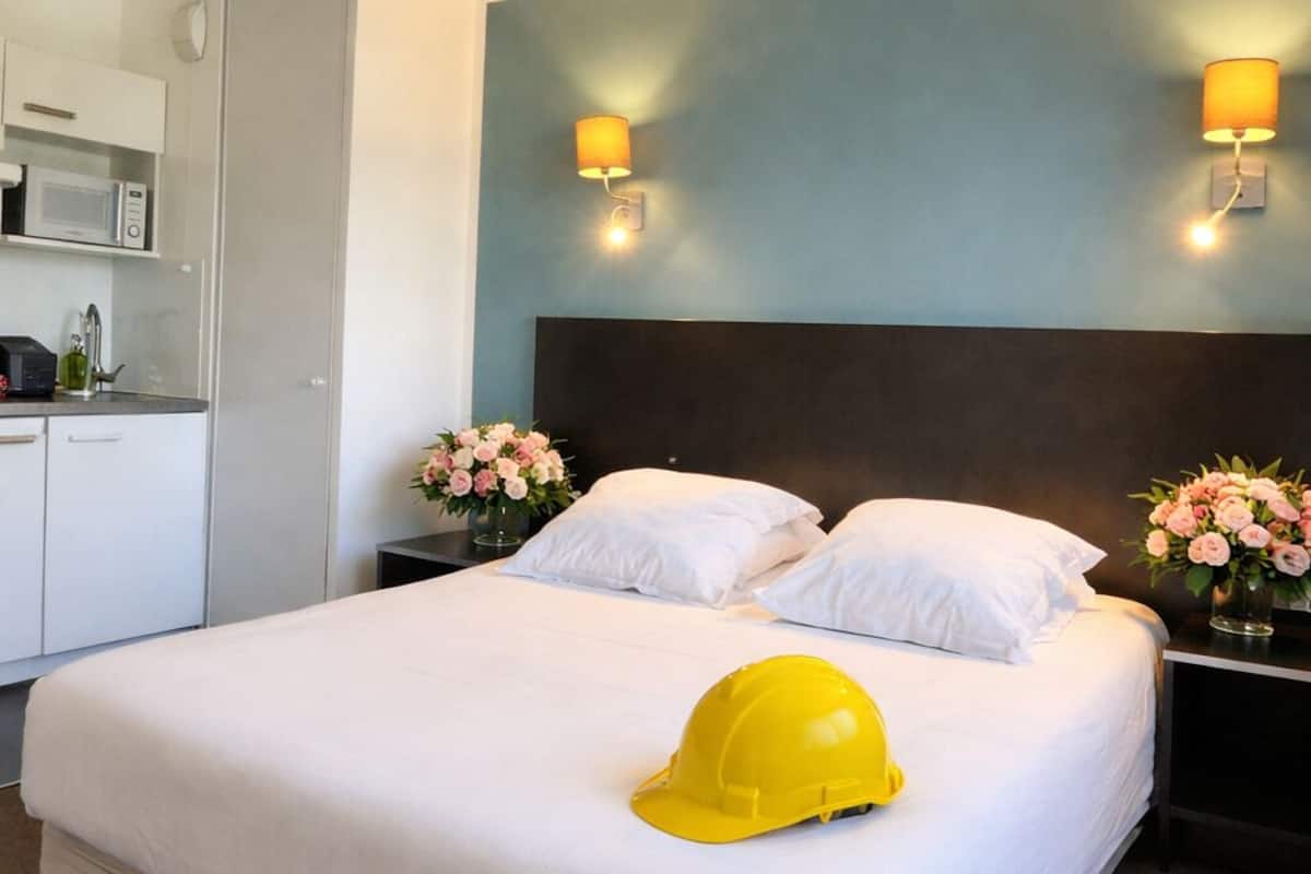 A hotel room with a bed, a nightstand, a lamp, a microwave, and a small kitchenette.