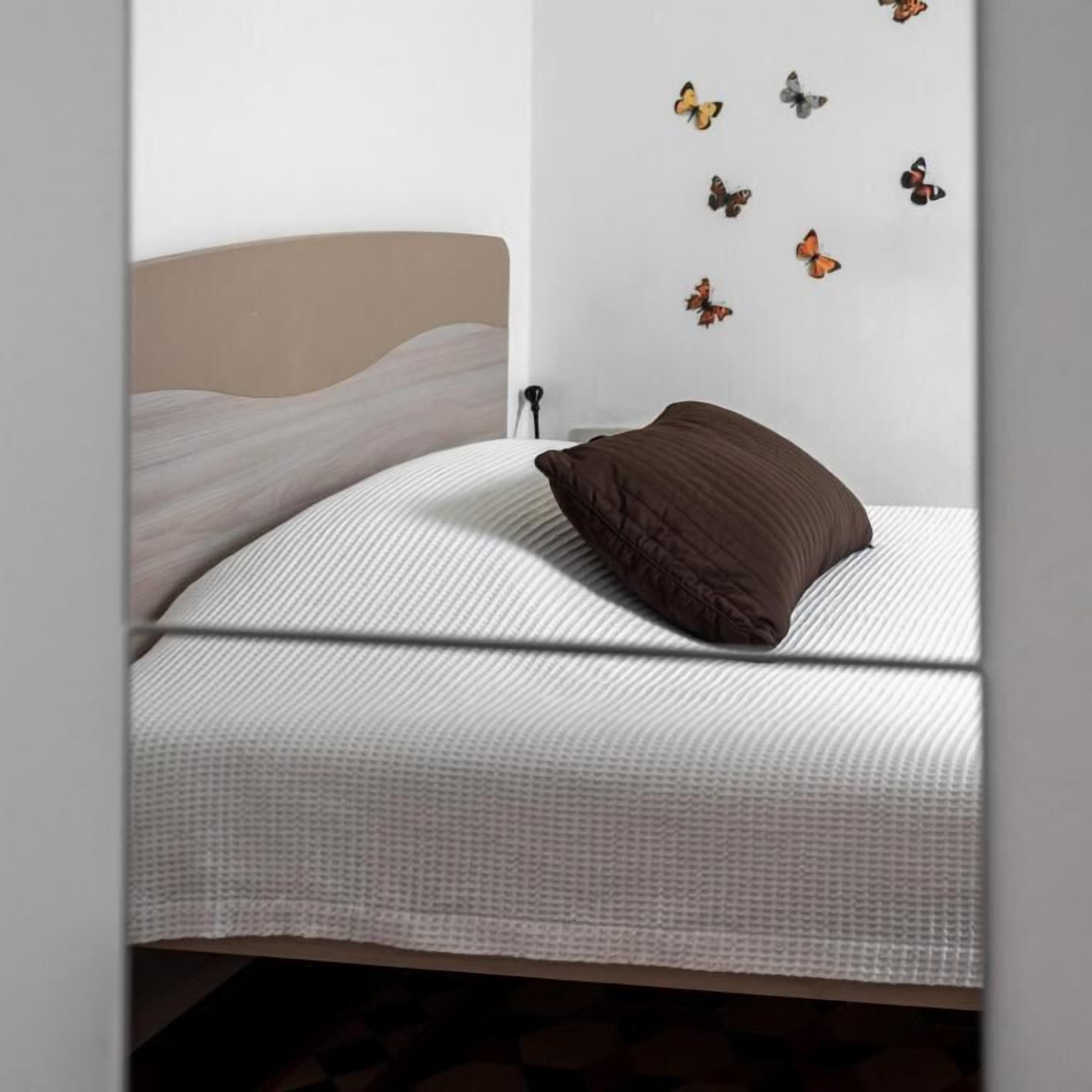 Un letto con una coperta bianca e testurizzata, un cuscino marrone e un muro decorato con adesivi a forma di farfalla.
