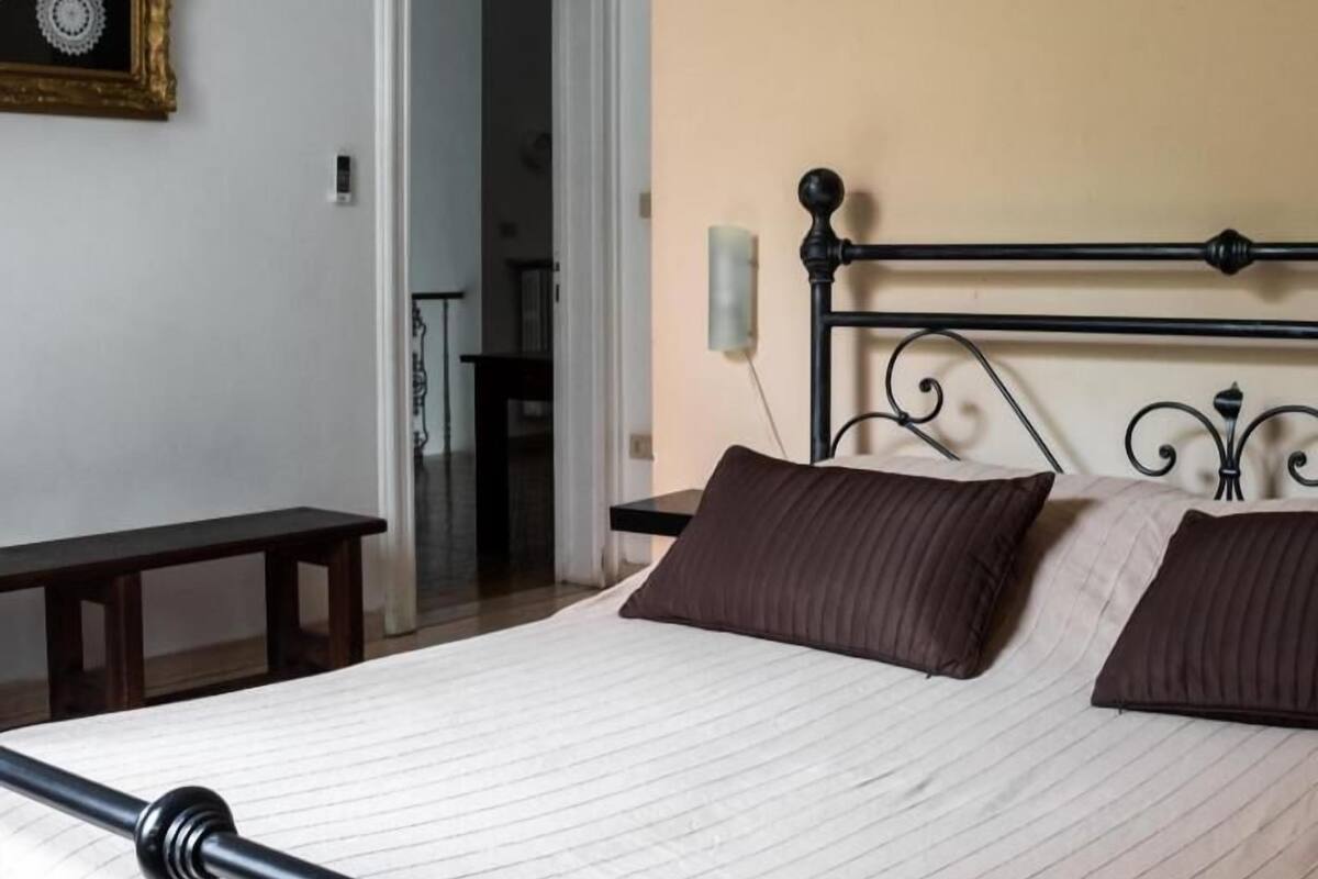 Une chambre à coucher avec un lit, une table de chevet, un tableau encadré au mur et une porte donnant sur une autre pièce.