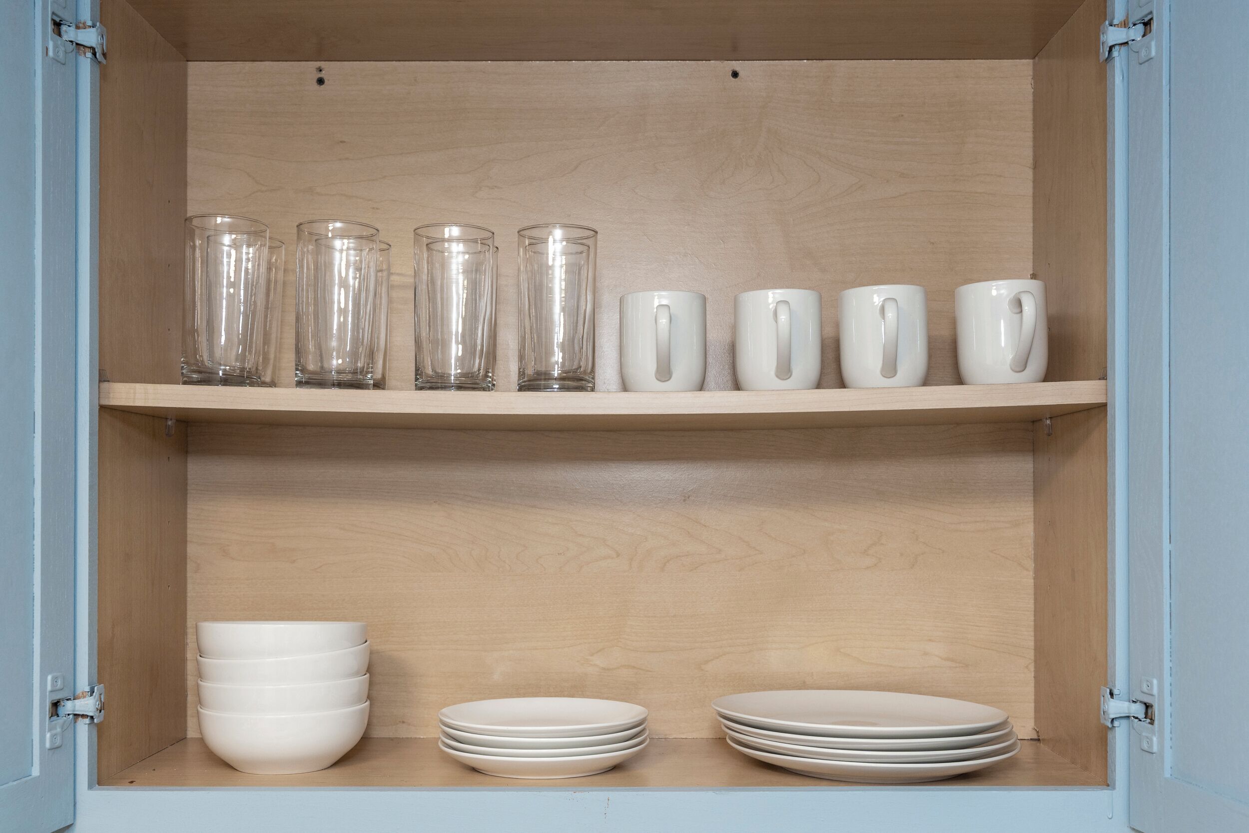 A wooden cabinet with clear glassware and white ceramic mugs on shelves.