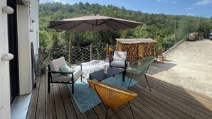 Una terraza de madera con muebles de exterior, una sombrilla grande y vistas a una ladera boscosa.