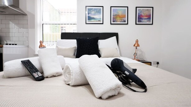 Habitación de hotel con cama, toallas, un control remoto, un secador de pelo e imágenes enmarcadas en la pared.