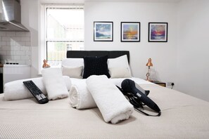 Quarto de hotel com cama, toalhas, controle remoto, secador de cabelo e quadros nas paredes.