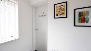 Una puerta blanca con un letrero que dice '10 Caemarfon Suite', una ventana con persianas y dos obras de arte abstractas enmarcadas en la pared.