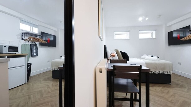 A compact hotel room with a bed, bedside table, and a small desk with a chair. There is a microwave and a trash bin in the kitchen area. - Contractor Studio • Parking • Smart TV & Kitchen (Pontardawe)