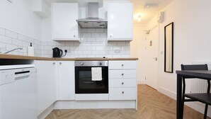 A compact kitchen with white cabinetry, a built-in oven, a dishwasher, and a wooden countertop. - Contractor Studio • Parking • Smart TV & Kitchen (Pontardawe)