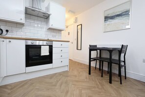 A kitchen with white cabinets, a black oven, a wooden countertop, a dining table with chairs, and a framed picture on the wall.