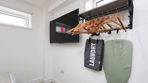 A laundry bag hanging on a wall-mounted rack, a green fabric item, and wooden hangers. - Contractor Studio • Parking • Smart TV & Kitchen (Pontardawe)