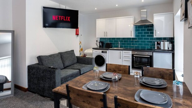 Una cocina moderna con armarios blancos, salpicadero verde azulado y un televisor de pantalla plana mostrando 'NETFLIX'.