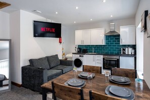 A modern kitchen with white cabinets, a teal backsplash, and a flat-screen TV displaying 'NETFLIX'. - Work Stay: En-Suite, Kitchen, Free Parking (Pontardawe)