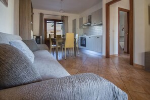 Un saló amb un sofà, una taula de dinar amb caires, una cuina i un passadís.