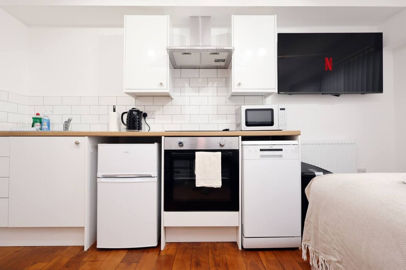 A compact kitchen with white appliances, a microwave, a kettle, and a TV displaying the Netflix logo.