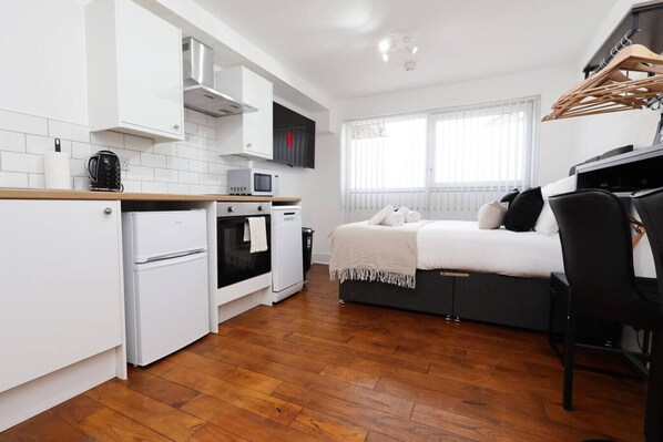 A compact room with a kitchenette, a bed, and a window.
