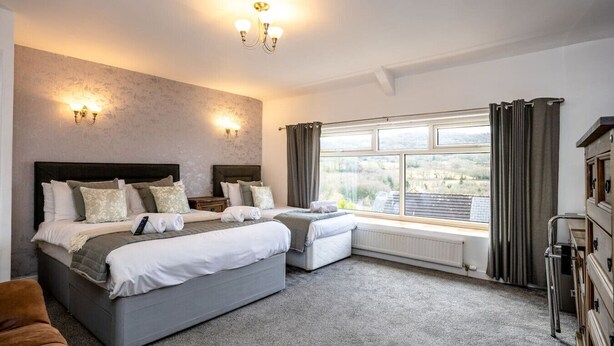 A bedroom with two beds, a large window with curtains, a radiator, and a dresser.