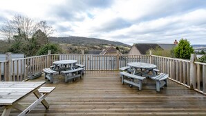 A wooden deck with picnic tables and a view of a hilly landscape.