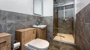 A modern bathroom with a glass shower enclosure, a wooden vanity, and a toilet.