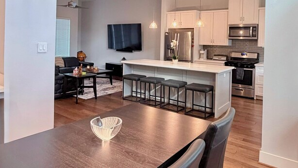 A modern kitchen with white cabinets, a central island with bar stools, and a dining area with a wooden table and chairs. - Urban Escape in the heart of Downtown Houston (Houston)