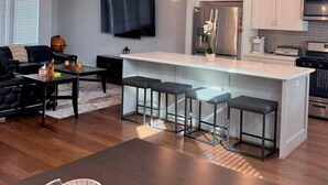 A modern kitchen with white cabinets, a stainless steel refrigerator, and a built-in oven. There is a dining area with a dark wooden table and bar stools. - Urban Escape in the heart of Downtown Houston (Houston)
