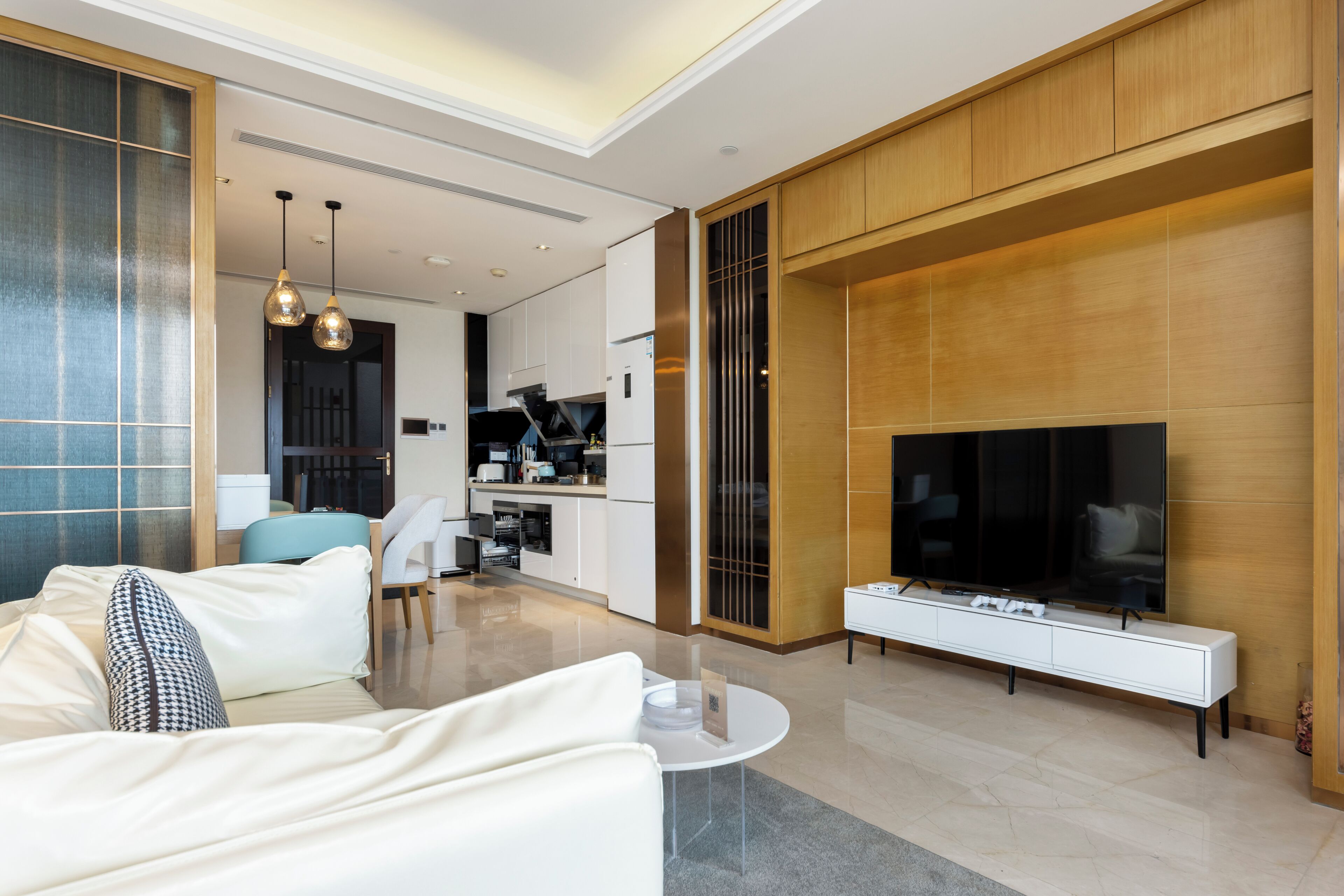 A modern living room with a sofa, coffee table, TV, and a kitchen in the background.