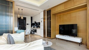 A modern living room with a sofa, coffee table, TV, and a kitchen in the background. - YanShe Oceanview Resort Haitang Bay (Sanya)