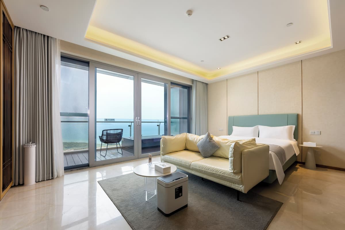 Una habitación de hotel moderna con cama, sofá, una mesita, un calefactor y un balcón con vistas.
