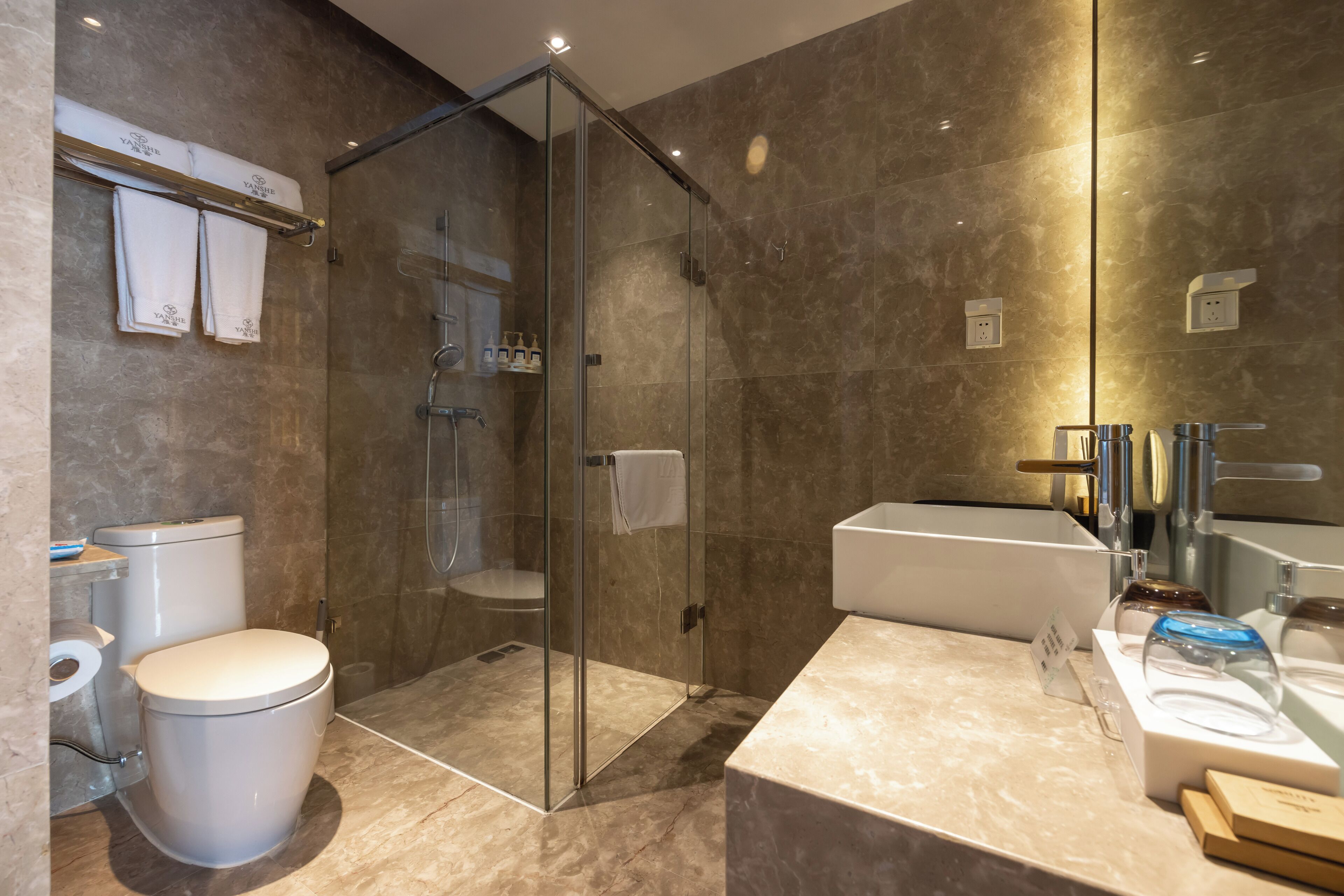 Un baño moderno con ducha envuelta en vidrio, inodoro, lavamanos y espejo.