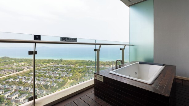 A balcony with a view of a residential area and the sea, a bathtub, and a glass railing. - YanShe Oceanview Resort Haitang Bay (Sanya)