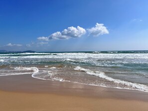 A beach with waves, a clear sky, and distant cityscape. - YanShe Oceanview Resort Haitang Bay (Sanya)