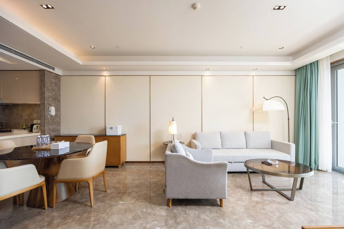 Una habitación de hotel moderna con comedor, sofá, mesa redonda de centro y lámpara.