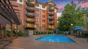 Un immeuble à plusieurs étages doté d’une piscine, d’un espace extérieur aménagé et d’une façade en pierre.