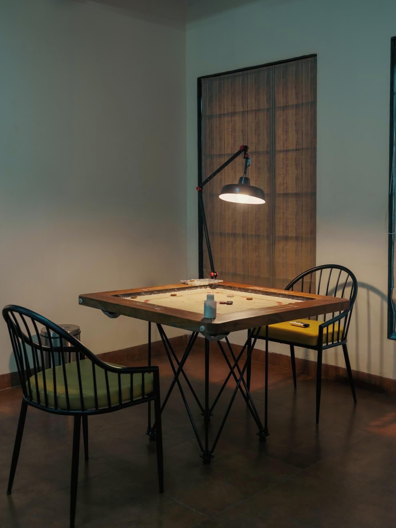 A dining table with chairs, a lamp, and a window with blinds.