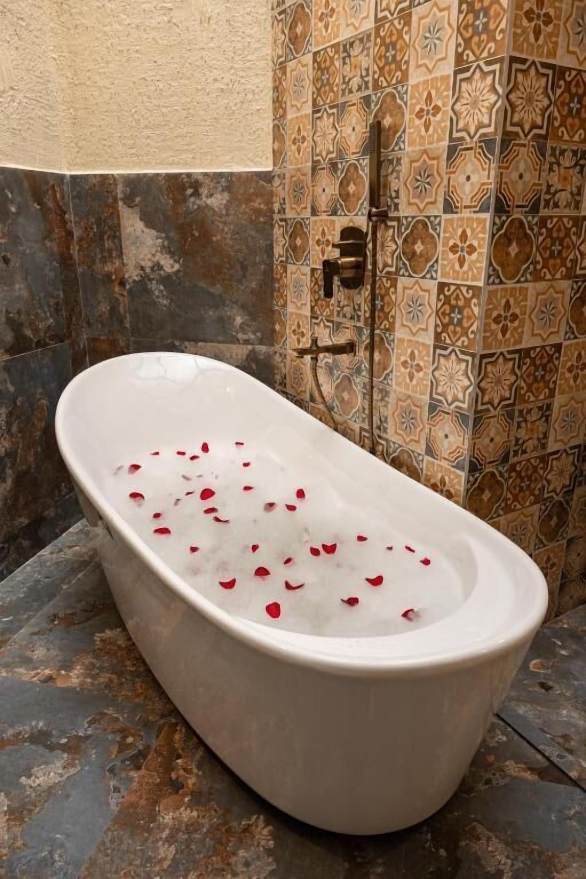 Una bañera con pétalos de rosa, ducha y baldosas con diseños.