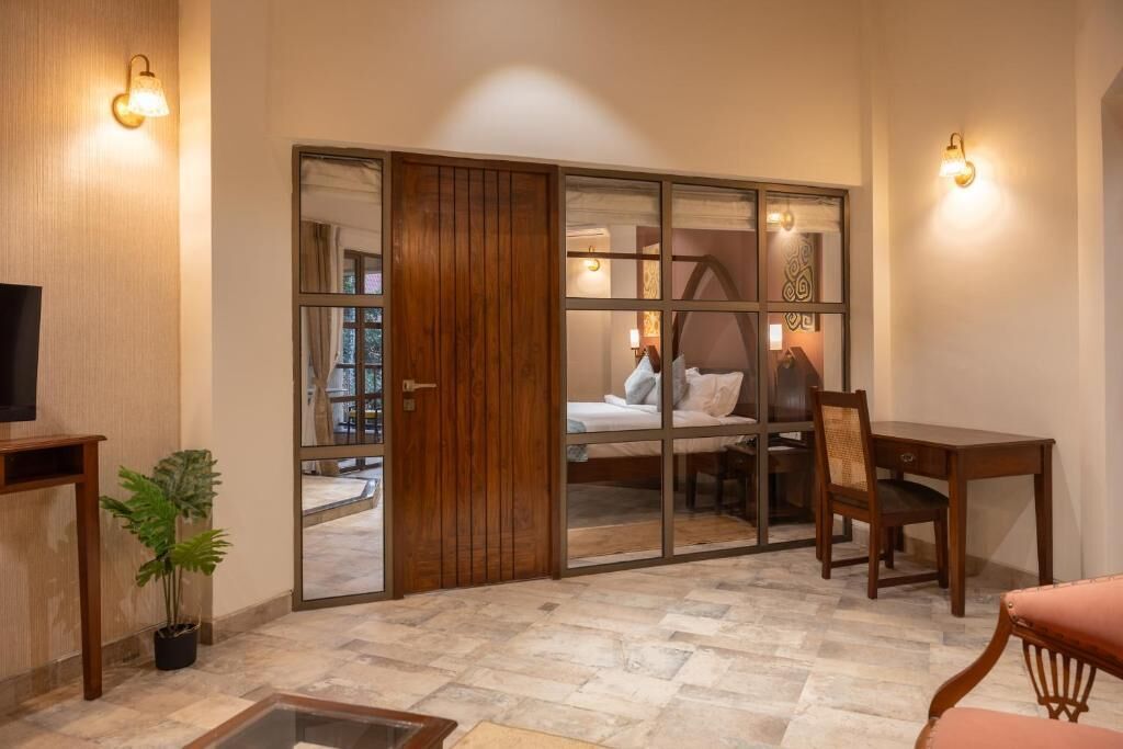 A room with a sliding door, a bed, a desk, a chair, a television, and a potted plant.