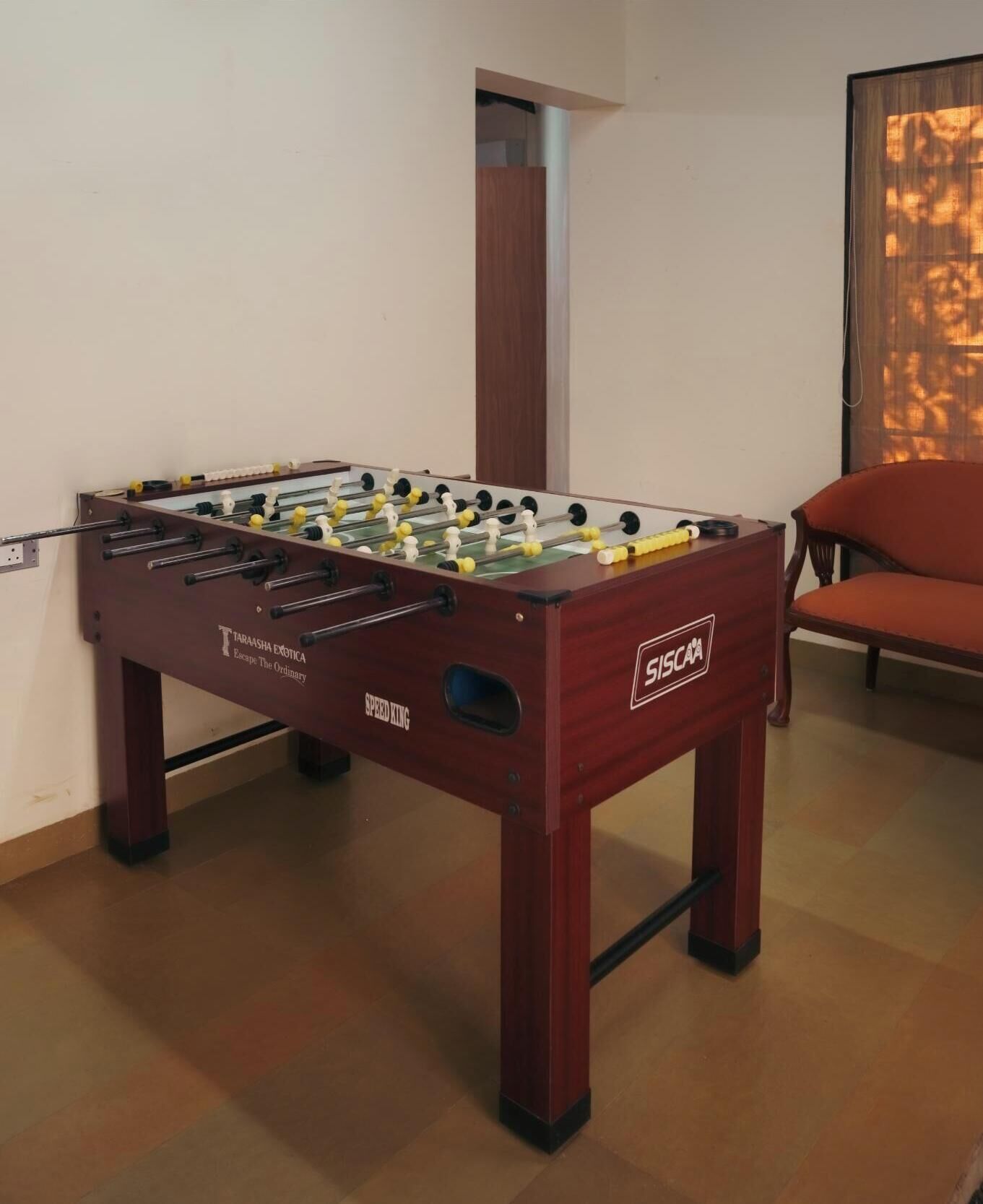 Une table de baby-foot dans une pièce avec une chaise en bois et une fenêtre équipée de stores.