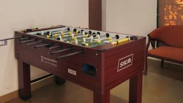 Une table de baby-foot dans une pièce avec une chaise en bois et une fenêtre équipée de stores.
