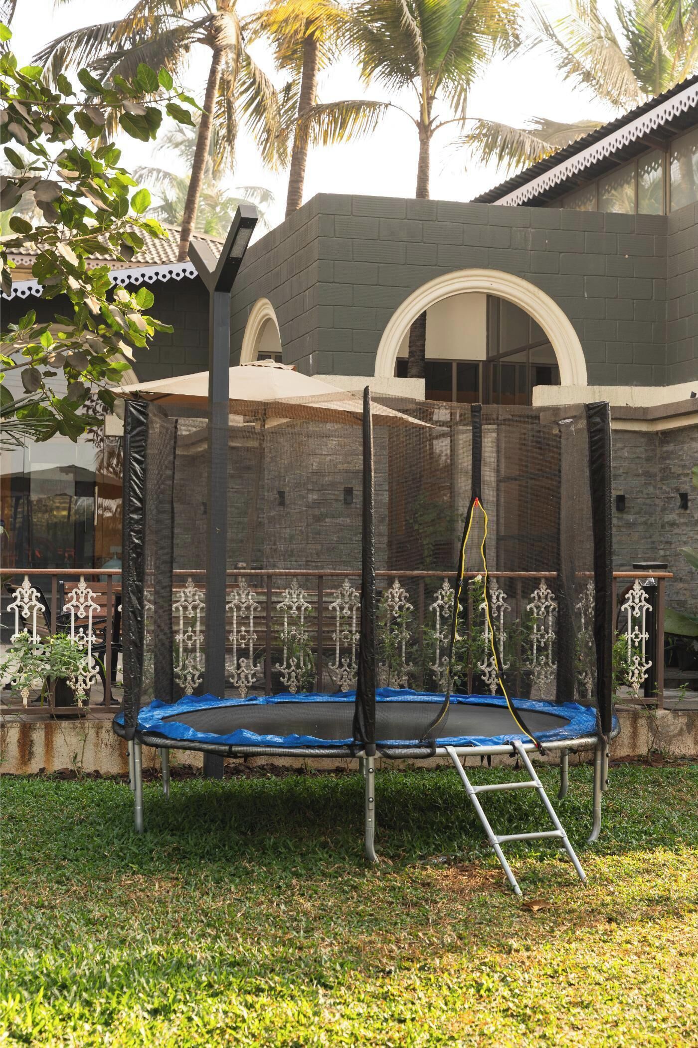 A trampoline with a safety net, a ladder, and a decorative fence in a backyard.
