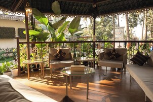 Un espacio al aire libre cubierto con mesas y sillas, rodeado de plantas en macetas y vistas al exterior.