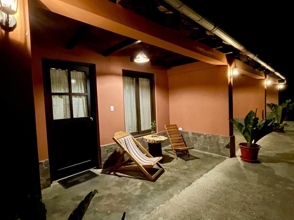 A building exterior with a black door, two windows, a concrete patio, and two wooden lounge chairs.
