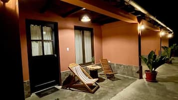 A building exterior with a black door, two windows, a concrete patio, and two wooden lounge chairs.