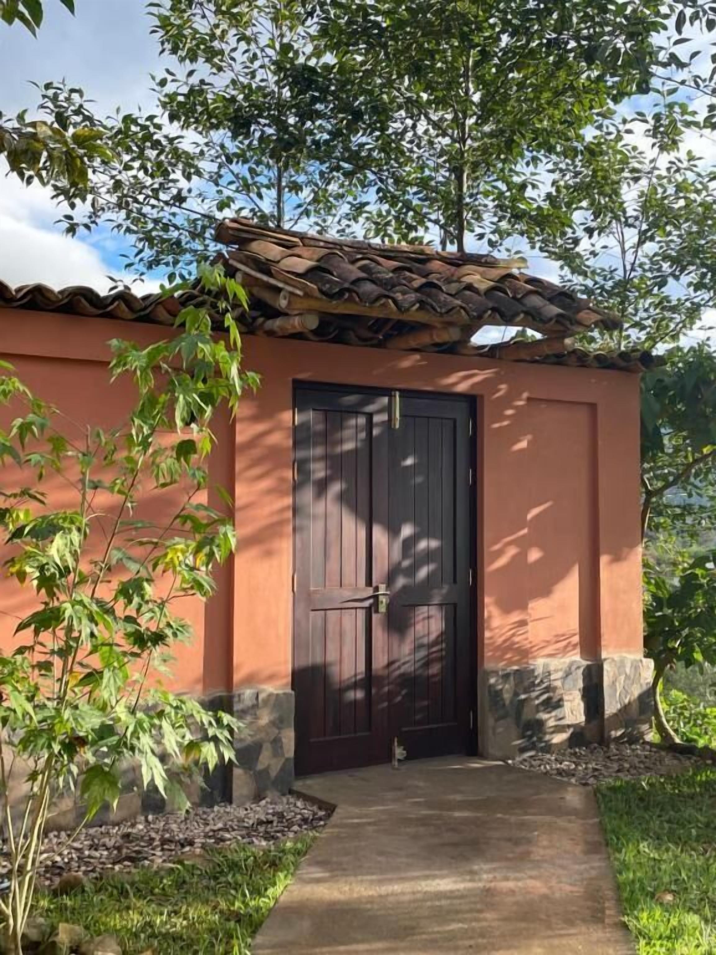 Un edificio con techo de tejas, puerta de madera oscura y un pequeño jardín con un sendero que lleva a la entrada.