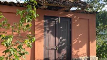 Un edificio con techo de tejas, puerta de madera oscura y un pequeño jardín con un sendero que lleva a la entrada.