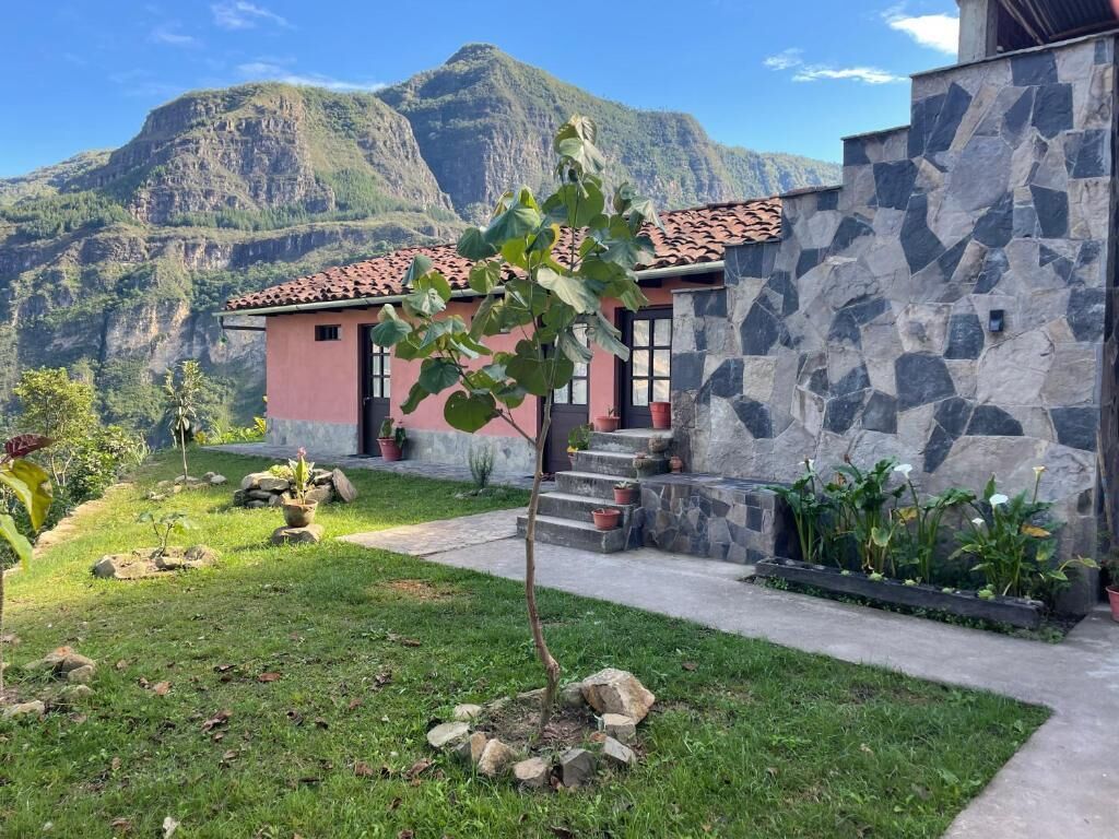 Una casa con un muro de piedra, un pequeño jardín y una montaña al fondo.