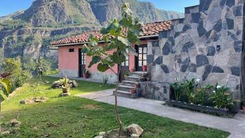 Una casa con un muro de piedra, un pequeño jardín y una montaña al fondo.