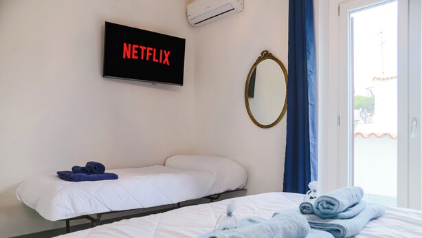 Ein Hotelzimmer mit Bett, einem Fernseher, der 'NETFLIX' anzeigt, einem Spiegel und einem Fenster mit Vorhängen.