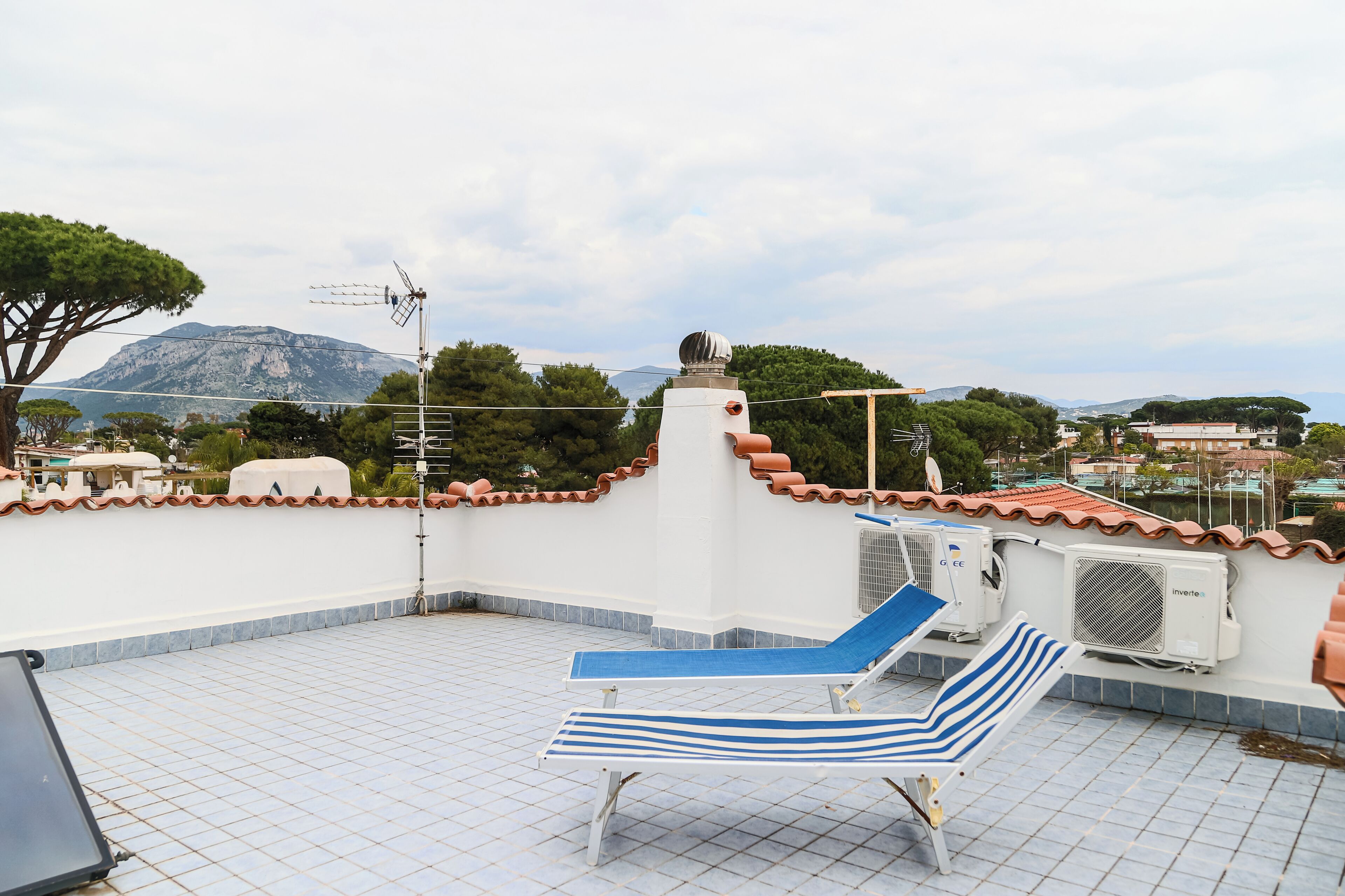Una terraza en la azotea con una silla de descanso, equipos de aire acondicionado y vistas a un paisaje montañoso.