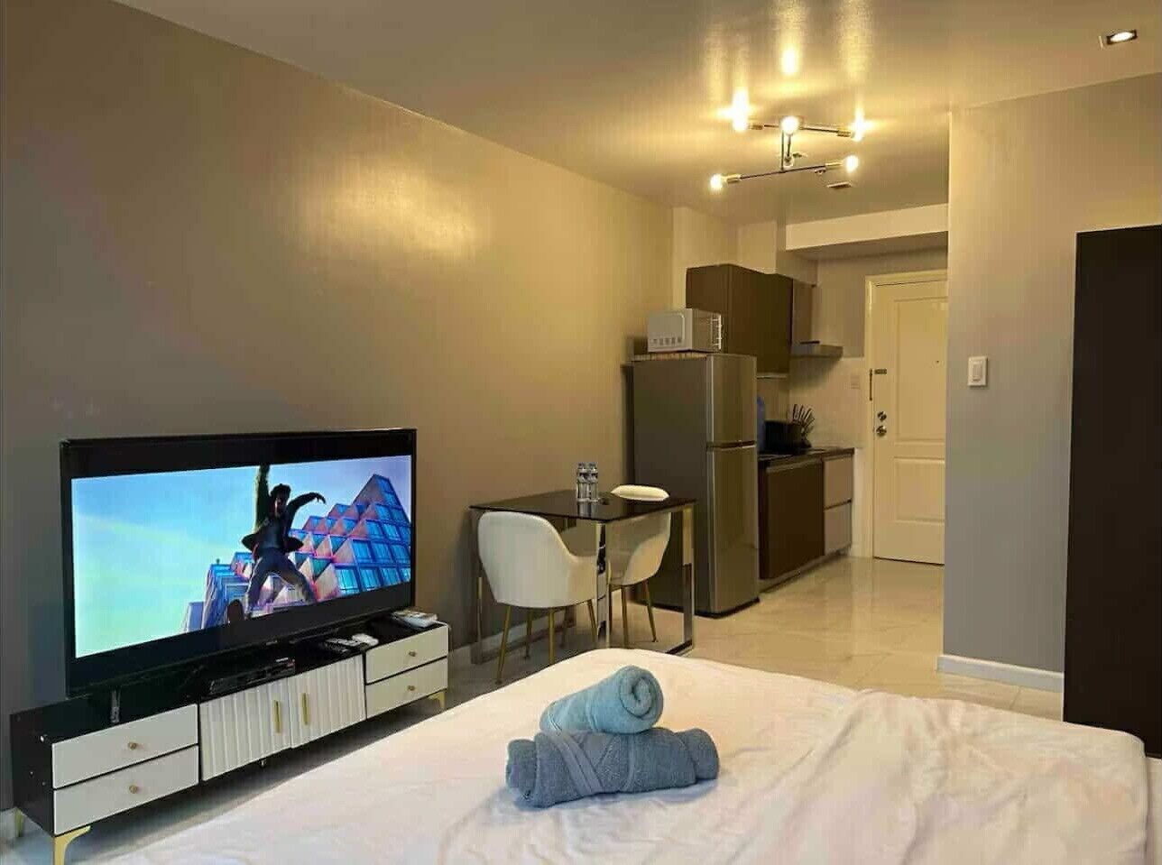 Ein Hotelzimmer mit Bett, Fernseher, Esstisch mit Stühlen, einer Küchenzeile und einer Tür.