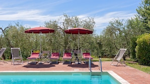 En pool med röda parasoller och solstolar.